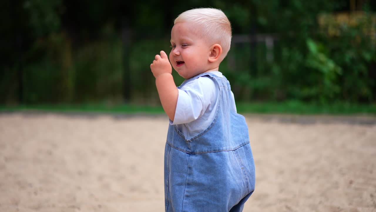 Sweet toddler boy walking by the sand picks an acorn. Happy child portrait. Baby on the walk in summer. Blurred backdrop.