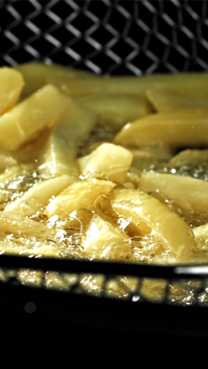 Patatine fritte dorate che friggono in olio bollente e ribollente