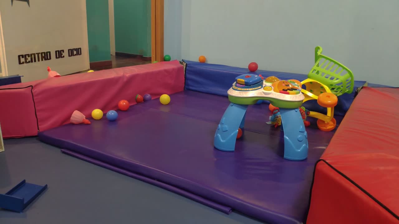 Gevarieerd speelgoed op de beschermde speelplaats met matten, poppen en gekleurde ballen, achteruit rijdend gefilmd, Ordenes, Galicië, Spanje.
