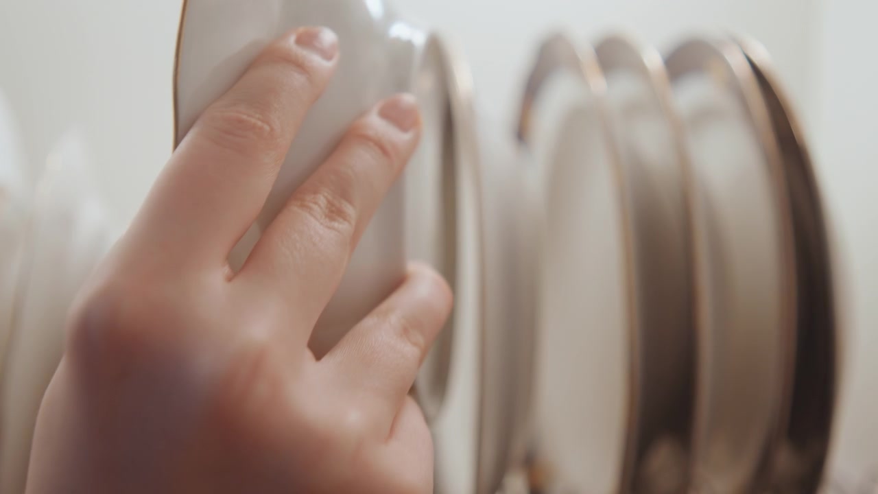 Closeup plates on drying rack, soft natural light, white porcelain stacked in metal rack, subtle water droplets, postcooking cleanup vibe, minimal neutral kitchen backdrop, focus on texture