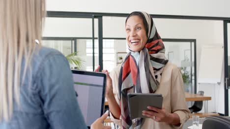 Happy-diverse-businesswomen-discussing-work-with-laptop-and-tablet-in-office-in-slow-motion