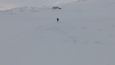 Young-girl-walks-on-snow-towards-abandoned-cabin,-winter-day