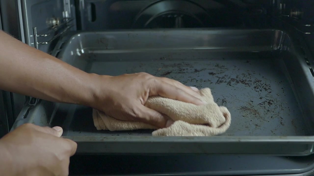 Person Cleaning Dirty Baking Tray Inside Oven