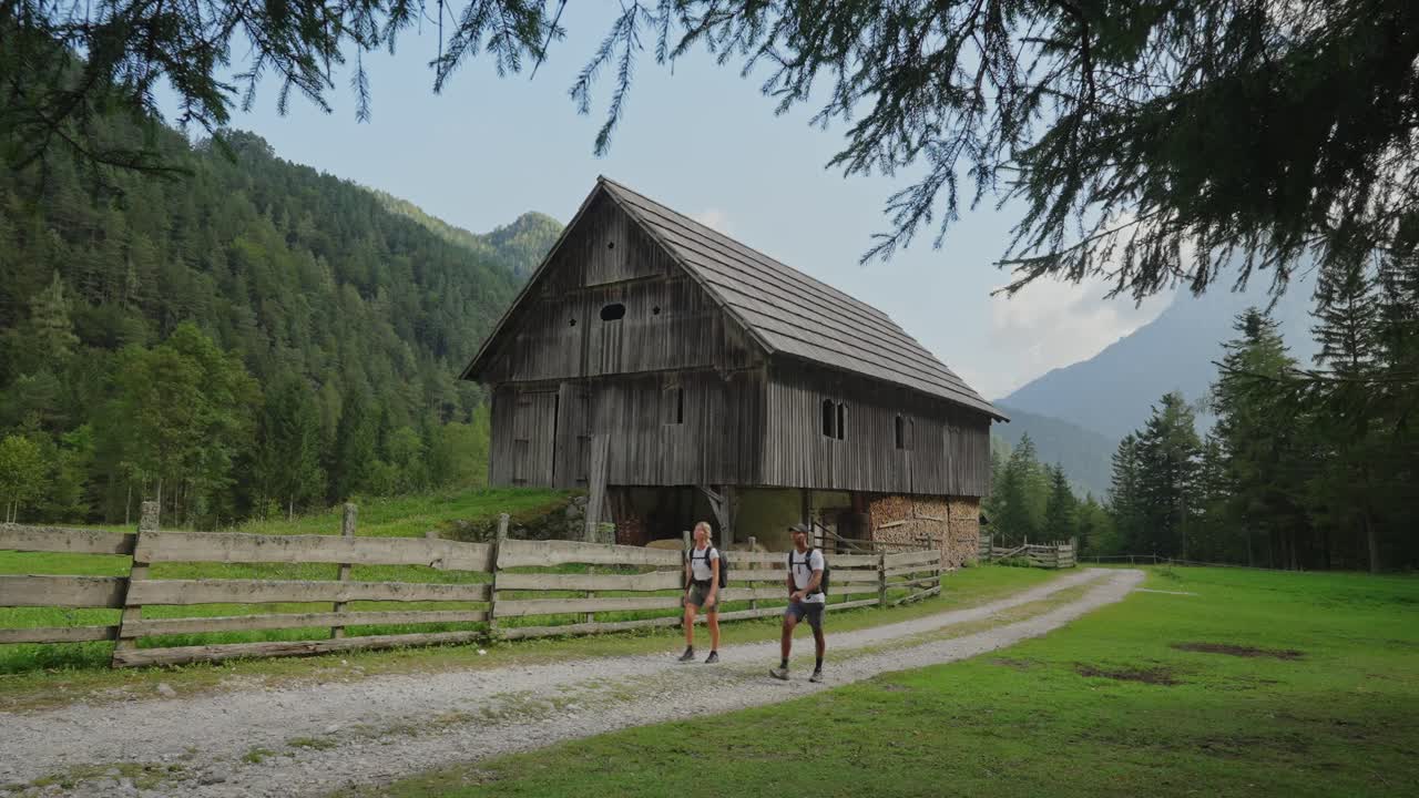 Couple hiking along a rustic barn surrounded by lush green forest and mountains