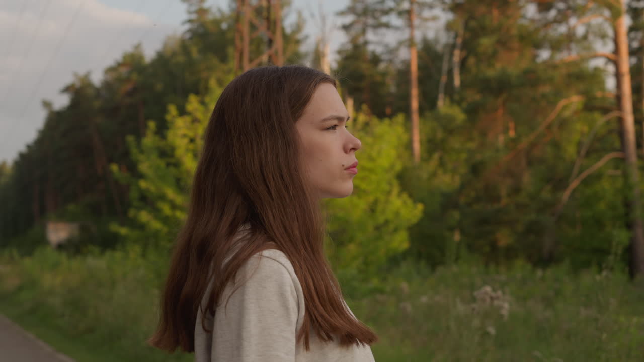 저녁에 숲 근처에 서있는 여자가, 젊은 여자가 다음으로 무엇을 할 것인지에 대해 좌절한 것처럼 보이며, 마음의 조화를 찾기 위해 신선한 공중에 혼자 고 있습니다.