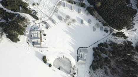 Aerial-Shot-Of-Alpine-Ski-Camp-In-Snow-Covered-Landscape-With-Cabins-And-Forest-Trees