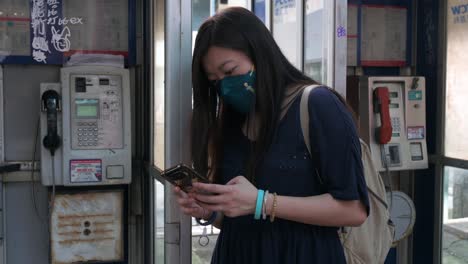 a woman uses a smartphone next to public telephone booths, also called a payphone, as they are rapidly dying out and disappearing in the age of smartphones and the internet