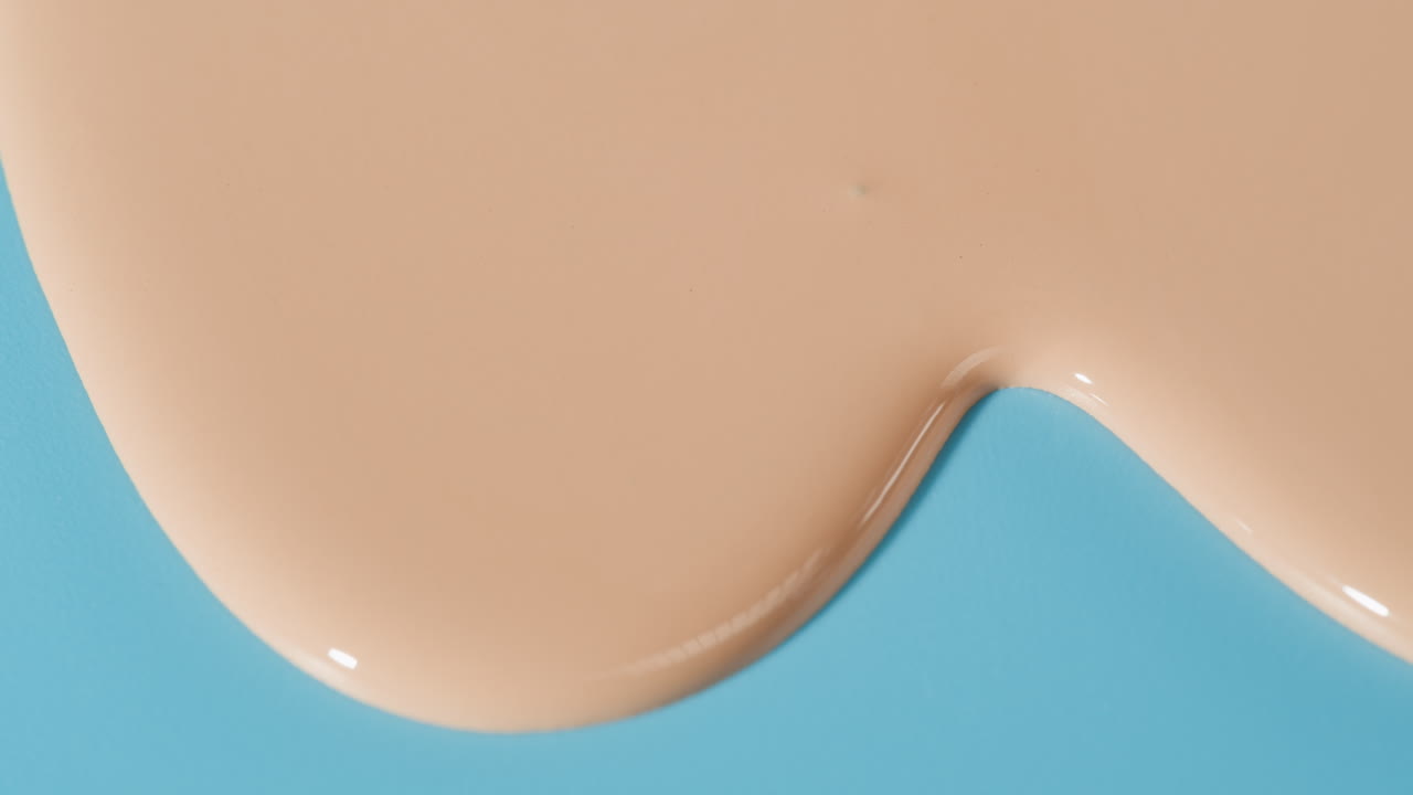 Fondotinta liquido beige che si spande su sfondo blu