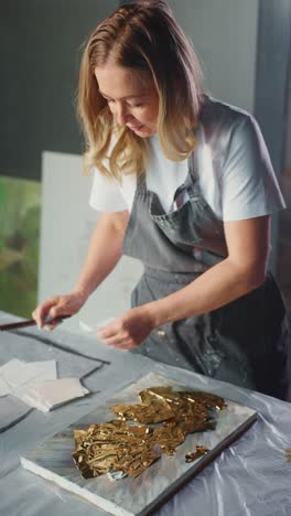 woman applying gold leaf to canvas in art studio