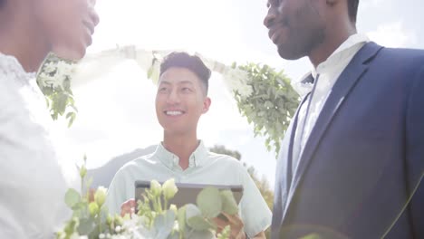 biracial man officiating marriage of happy african american couple in sunny garden, in slow motion