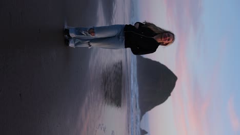 rubia, joven feliz modelando por la roca del pajar en la playa de cañones, oregón