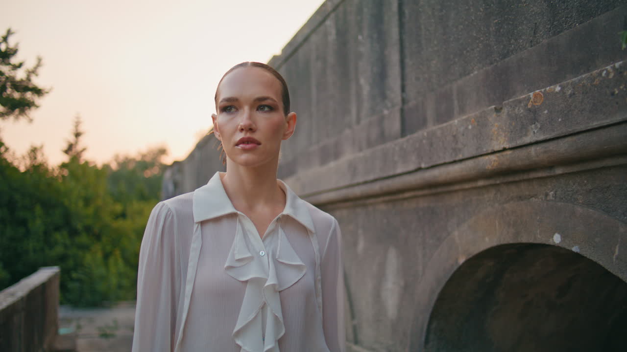 평온한 여자가 여름 저녁에 중세 시대의 돌로 지어진 건물을 걸어다니고 있습니다.