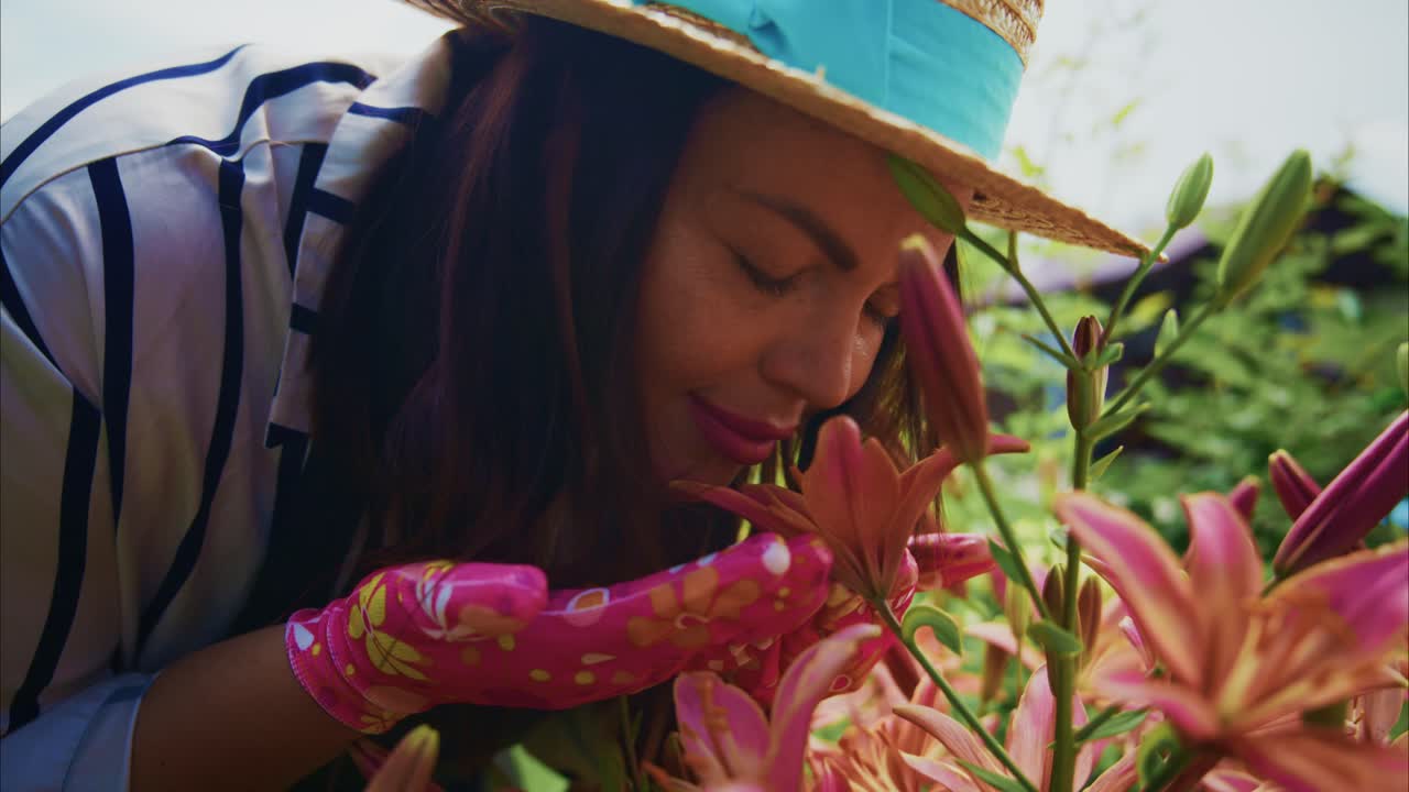 Woman in straw hat enjoying fragrant flowers in a vibrant garden with colorful blooms surrounding her