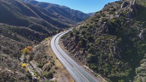 drone flying over curvy road in between mountains