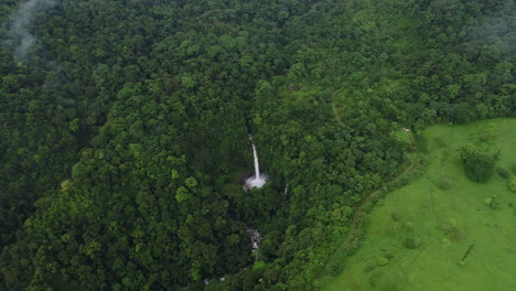 aerial over dense tropical rain forest with tall waterfall coming from cliff, 4k