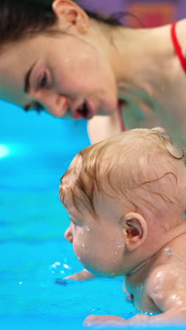 caucasian woman holding a baby in the pool on her palm. infant child is taught to swim. vertical video