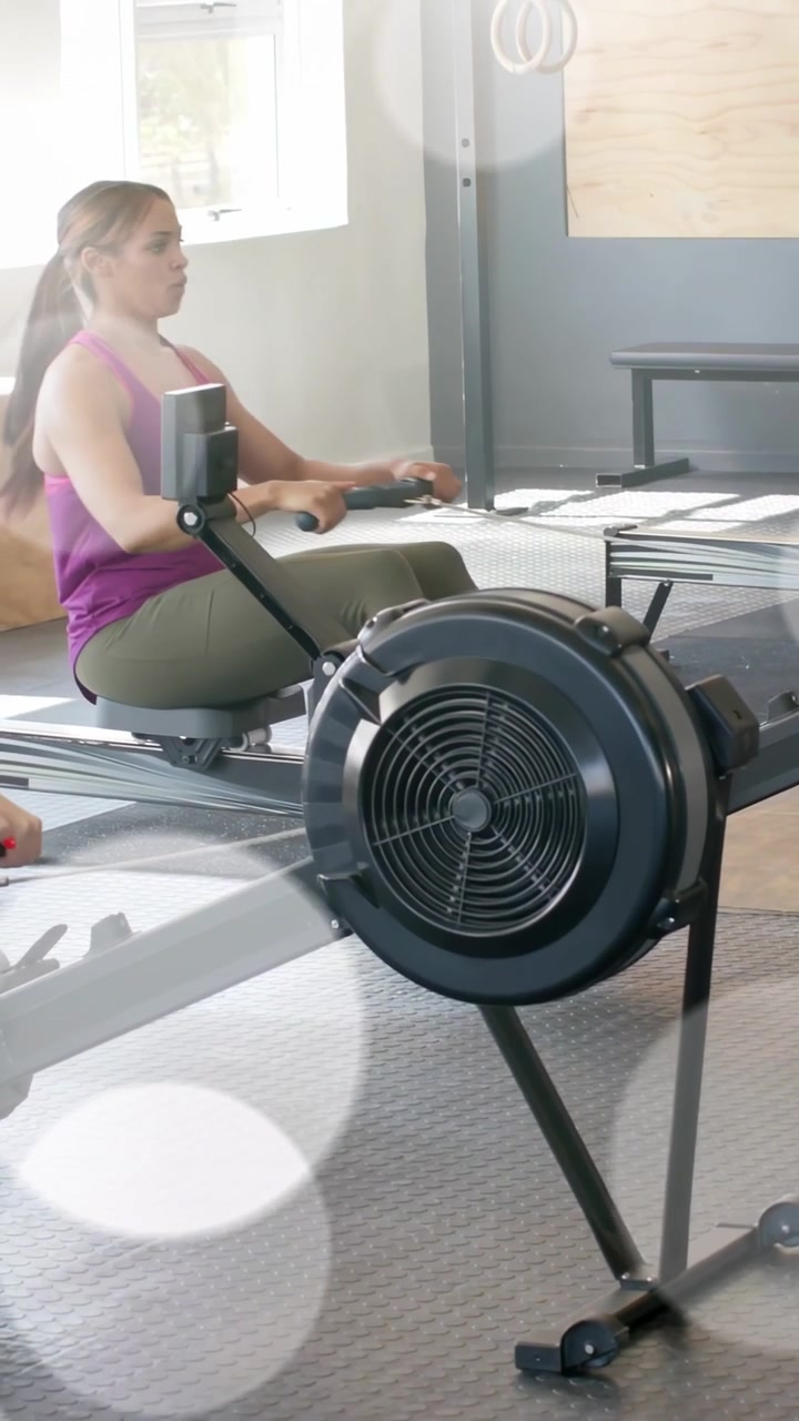 Vertical video: Woman gripping handle, spinning flywheel with animated lines, rowing for fitness