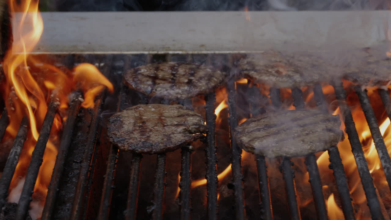 Hamburger su barbecue a carbone untuoso e fumoso in un pomeriggio estivo su griglia commerciale al rallentatore