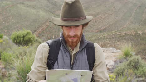 Superviviente-Masculino-Caucásico-Barbudo-En-La-Montaña-En-El-Desierto,-Leyendo-El-Mapa-Y-Mirando-A-Su-Alrededor