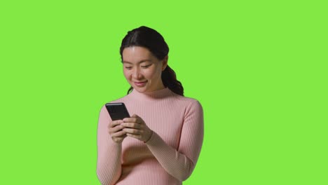 studio shot of woman smiling and laughing at message or content on mobile phone against green screen 1