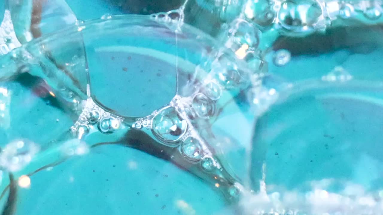 Detailed view of transparent bubbles and foam interacting on a vibrant blue water surface.
