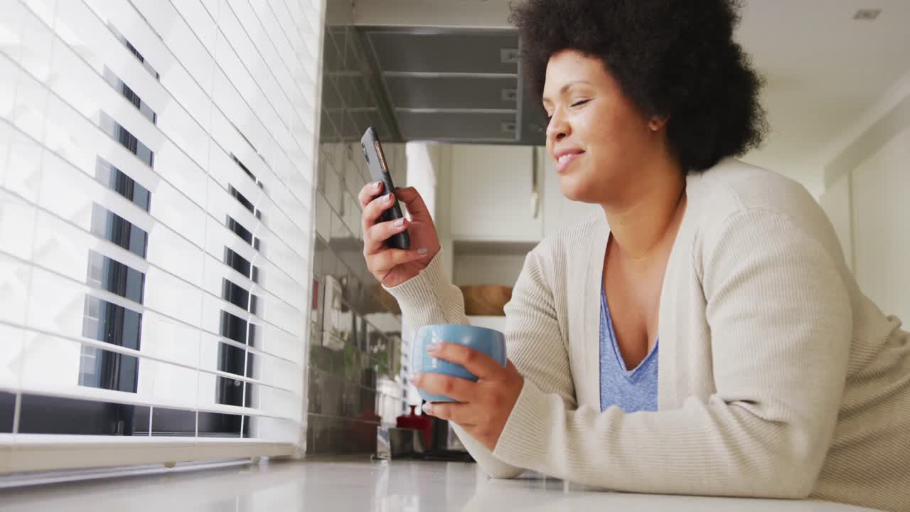 Video di una felice donna afroamericana curvy che beve caffè e usa lo smartphone