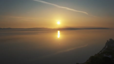 drone flying above a  golden misty sea shore on golden hour sunset, aerial over misty water surface in lesvos, greece.