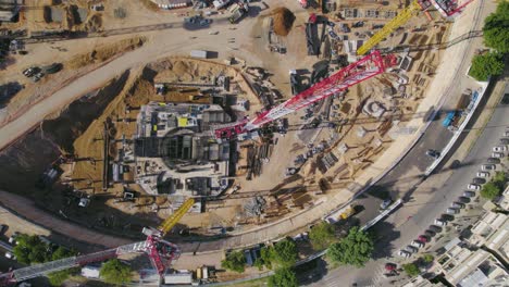 Von-Oben-Nach-Unten-über-Turmdrehkran-Auf-Einer-Baustelle-Auf-Einem-Großen-Stadtplatz,-Während-Autos-Vorbeifahren