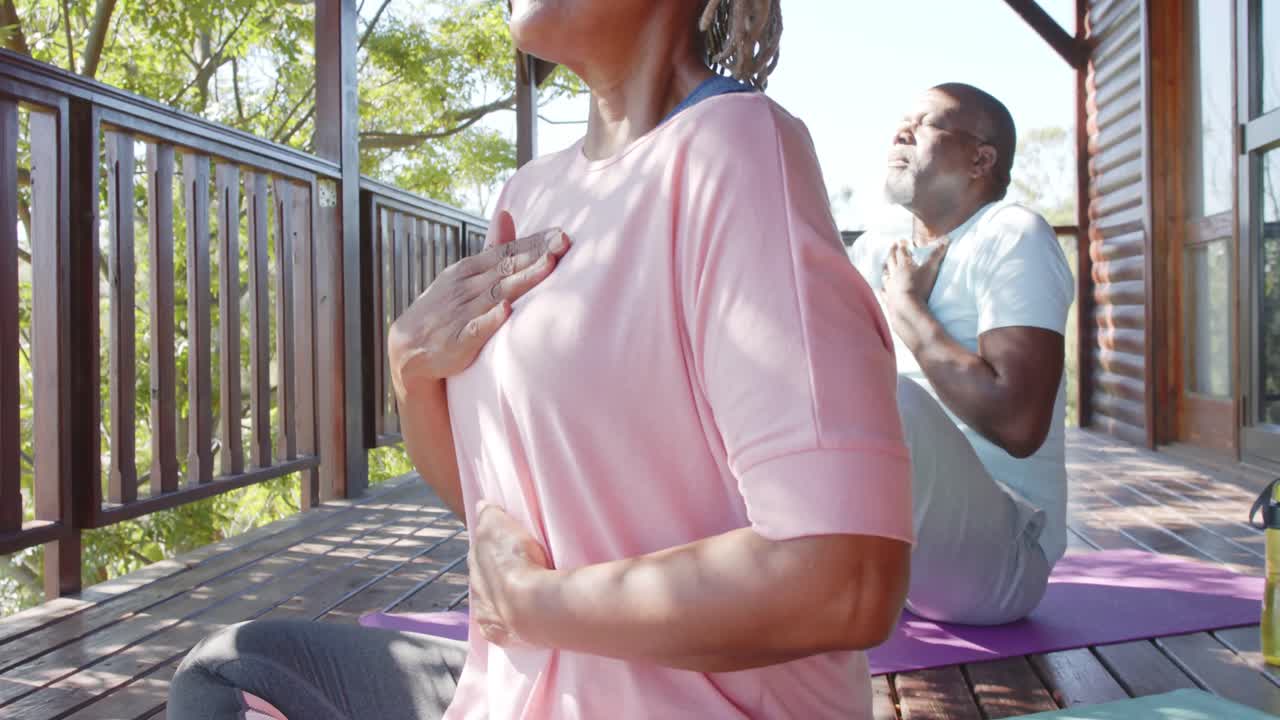 초점을 맞춘 아프리카계 미국인 부부가  ⁇ 은 테라스에서 요가 연습을 하고 있습니다.
