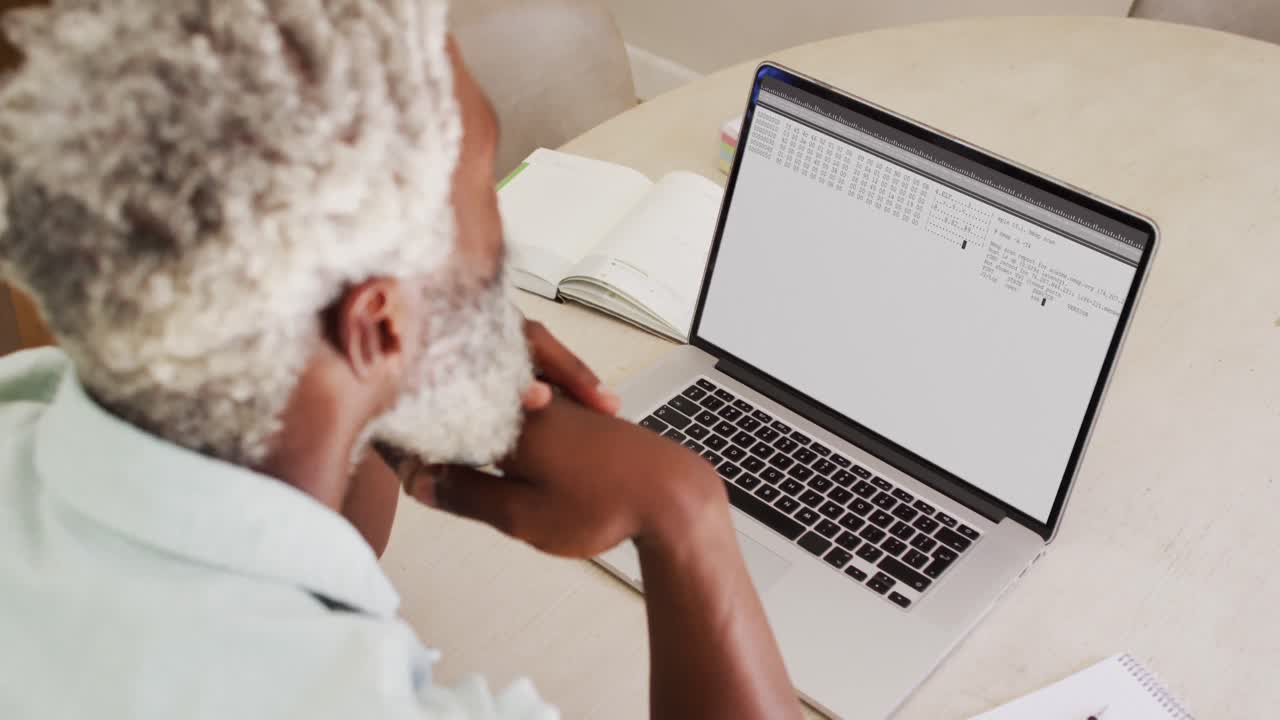 Uomo afroamericano seduto alla scrivania che osserva la codifica e l'elaborazione dei dati sullo schermo del laptop.