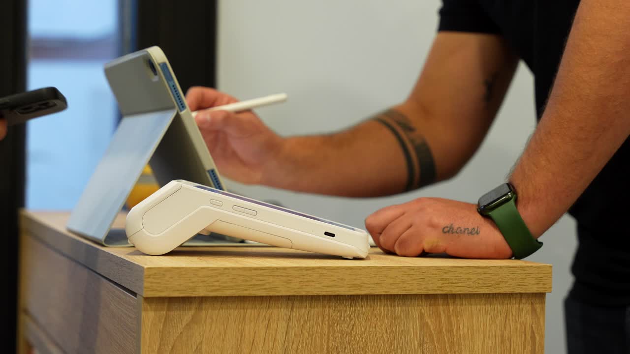 Close up of customer paying with phone on dataphone as barber takes notes on tablet