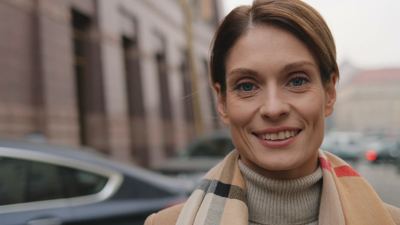 Camera zoom on Caucasian businesswoman looking at the camera and smiling in the street in autumn