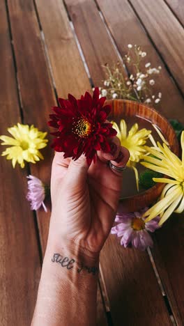 woman holding a red flower on a wooden table with other flowers