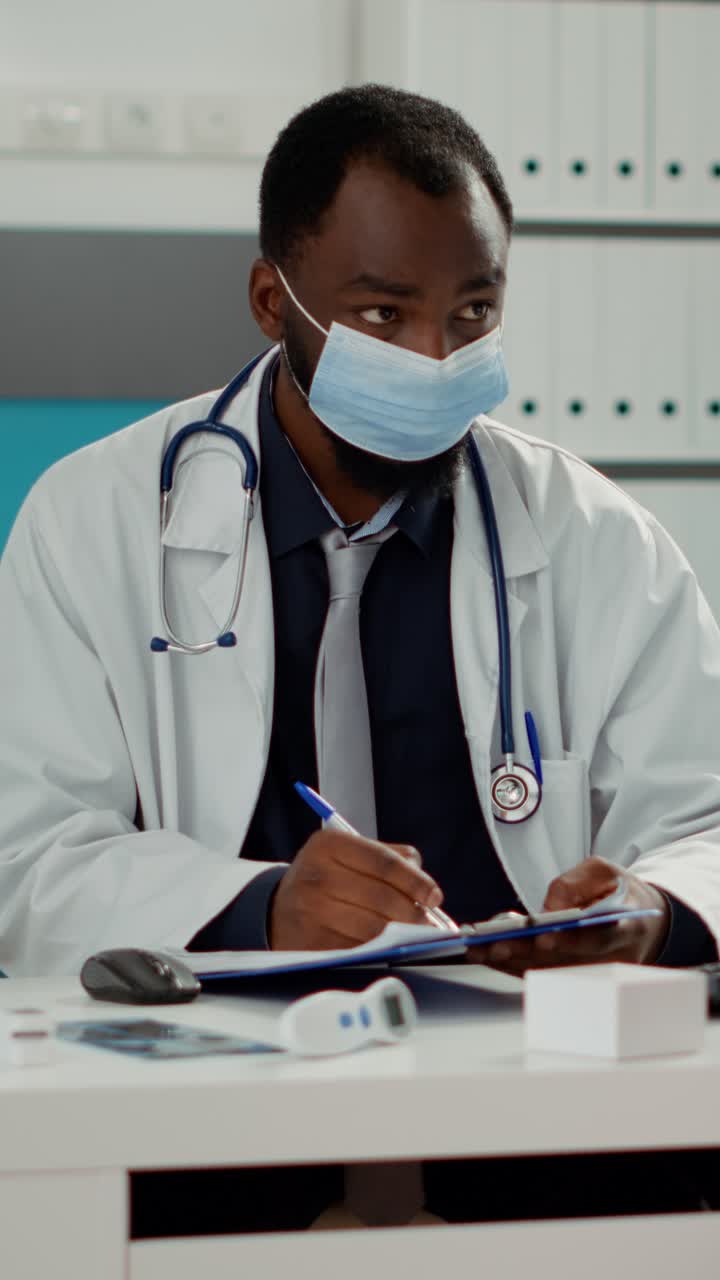 Doctor wearing a mask taking notes in his office