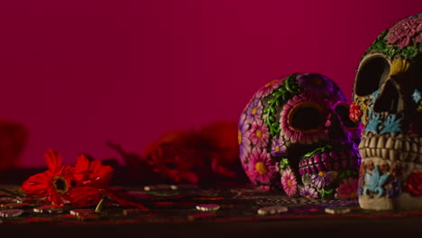 close up of decorated skulls and flowers celebrating mexican holiday of dia de muertos or day of the dead against red background