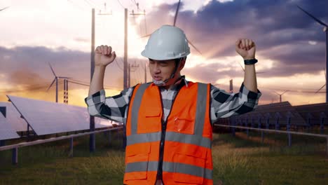 asian male engineer with safety helmet screaming goal and dancing celebrating with solar panel and wind turbines