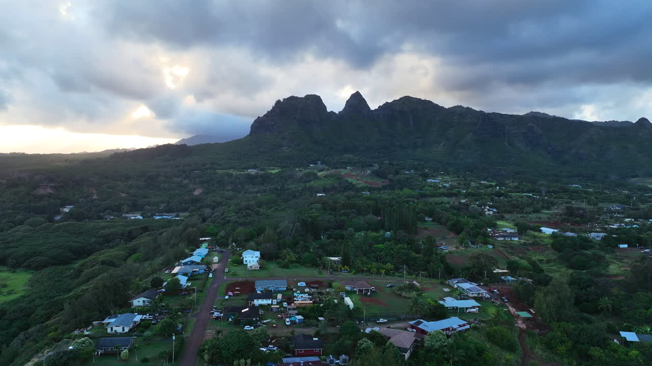 Aerial tracking shot of a Hawaiian town and mountains of Kauai, moody evening