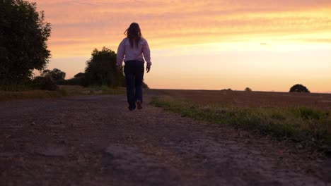 Frau-Geht-Auf-Staubiger,-Trockener-Straße-In-Den-Sonnenuntergang,-Weitwinkelaufnahme