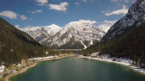 Perfect-snow-covered-forest-banks-around-Plansee-lake-aerial-view-towards-Austria-mountains-landscape