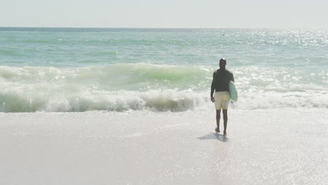 Hombre-Afroamericano-Senior-Caminando-Con-Tabla-De-Surf-En-La-Playa-Soleada
