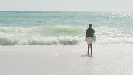 Älterer-Afroamerikanischer-Mann,-Der-Mit-Surfbrett-Am-Sonnigen-Strand-Spaziert