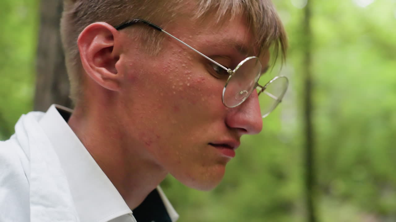Portrait view young botany student in white shirt carefully putting glasses in forest surrounded by blurred trees, reflecting concentration and calmness during outdoor study in natural environment