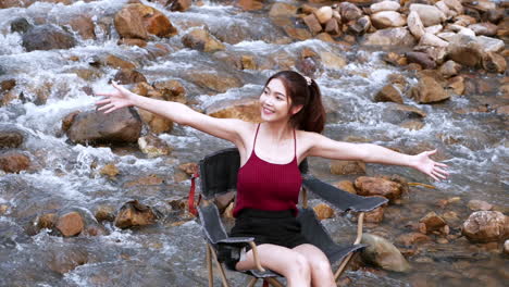 mujer asiática de rojo sentada en una silla con grandes rocas y agua salpicando lentamente para relajarse y ser feliz en las vacaciones de verano