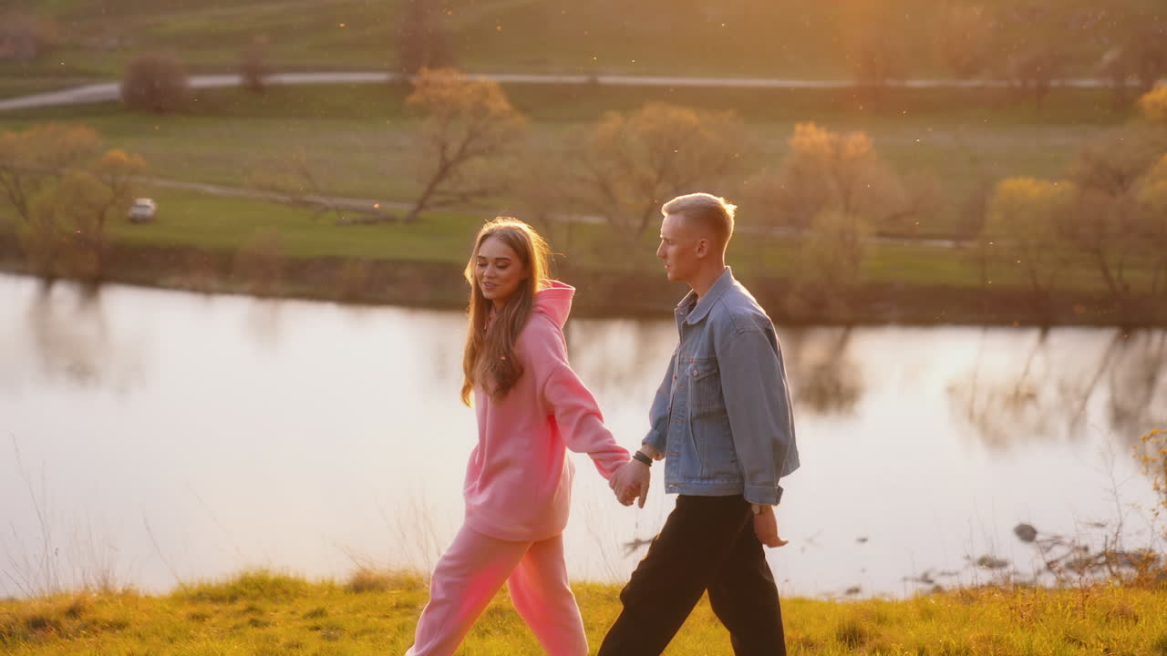 Young man and woman spending time together outdoors. Couple holding hands are walking near the river with happiness.
