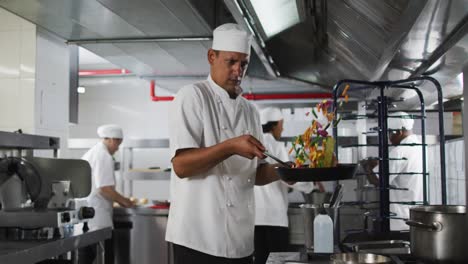 cocinero de raza mixta fritando verduras en sartén en la cocina de un restaurante