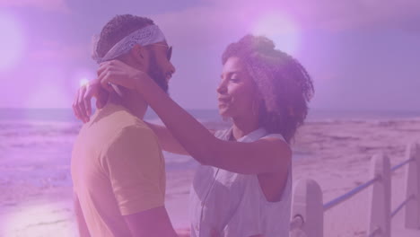 animation of light spots over biracial couple embracing at beach