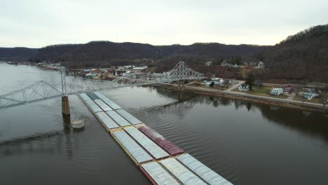 Below-the-Black-Hawk-Bridge-at-Lansing,-Iowa,-a-towboat-pushes-barges-north-on-the-Mississippi-River-1