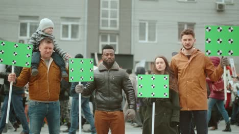 diverse crowd of protesting people at rally with greenscreen mockup banners.