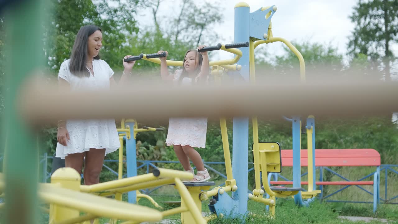 una madre embarazada y su hija joven disfrutan de un tiempo de juego juntos en un patio de recreo en el parque, rodeados de árboles y vegetación
