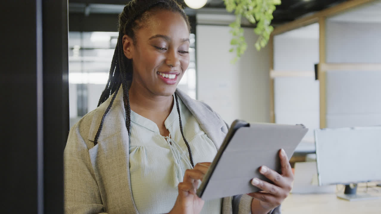 Happy african american casual businesswoman using tablet standing in office, slow motion
